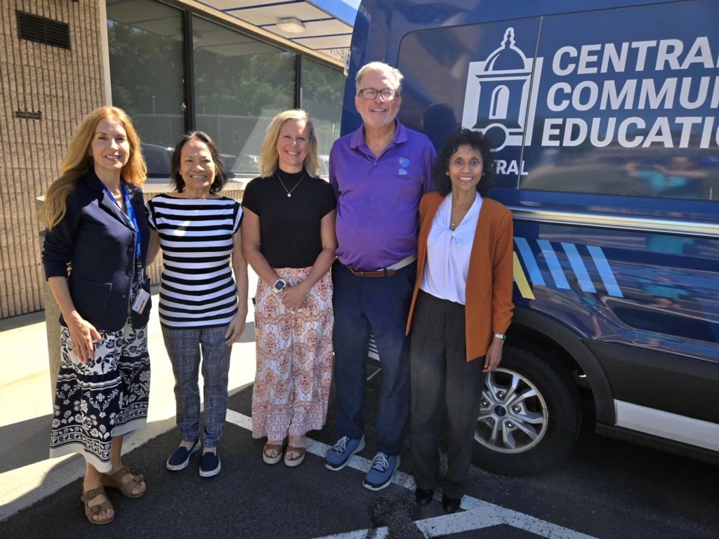 Five people smiling together outdoors in front of a Central Community Education van.